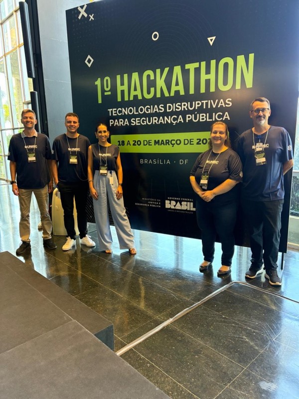 Grupo premiado tendo ao fundo banner do evento Hackathon